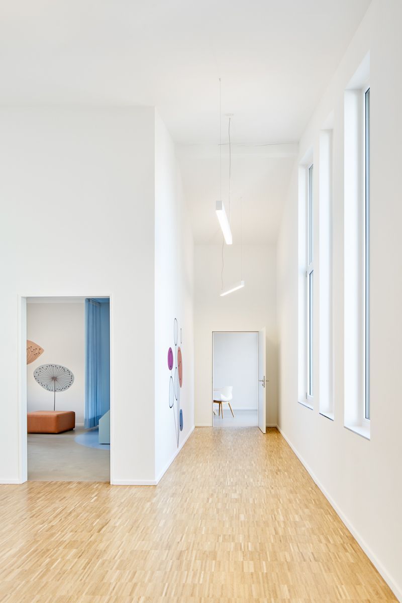 Heller, minimalistischer Flur in einem Krankenhaus mit großen Fenstern und Holzfußboden. Die Gestaltung der Räume fördert Ruhe und Wohlbefinden im Rahmen von New Work.