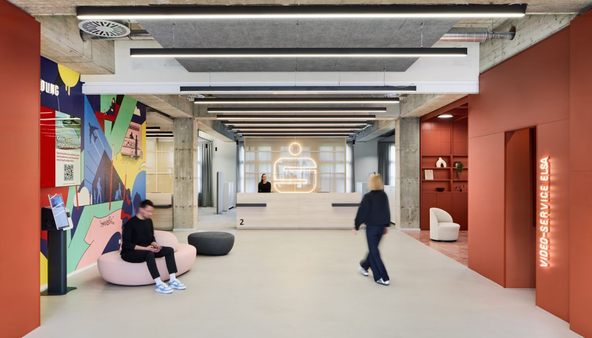Ein Empfangstresen aus Holz und warme Rottöne heißen die Besucher der Stadtsparkasse Düsseldorf Willkommen | Bank Architekt bkp